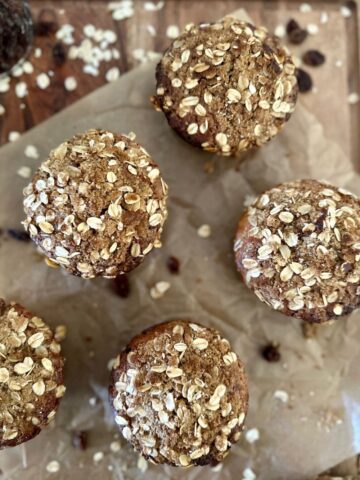 sourdough oatmeal raisin muffins sitting on a sheet of parchment paper. There are some rolled oats and raisins scattered around the muffins.