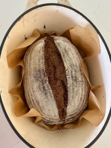 Loaf of sourdough pumpernickel bread that has been baked in a cream enamel Dutch Oven.