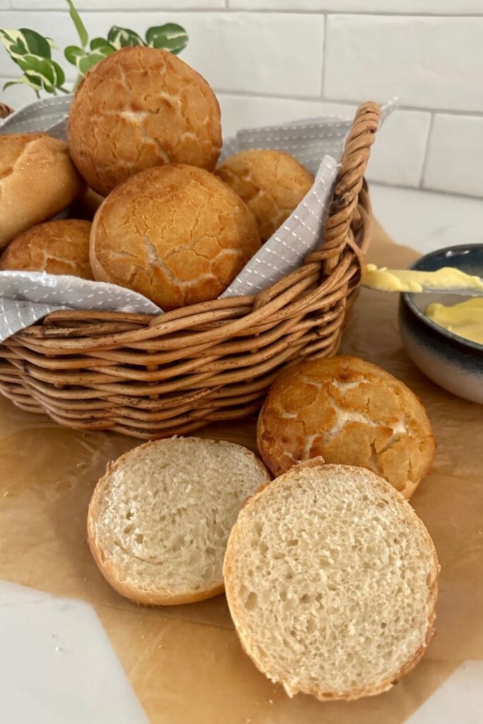 Sourdough Tiger Roll that has been cut open to show the soft inside. There is a basket of sourdough tiger rolls sitting in the background.