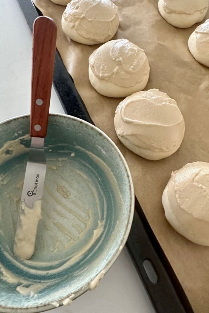 A blue bowl that has had the rice flour paste for the top of sourdough tiger rolls in it. You can see an offset spatula sitting on top of the bowl and some of the dough balls spread with the paste in the background.