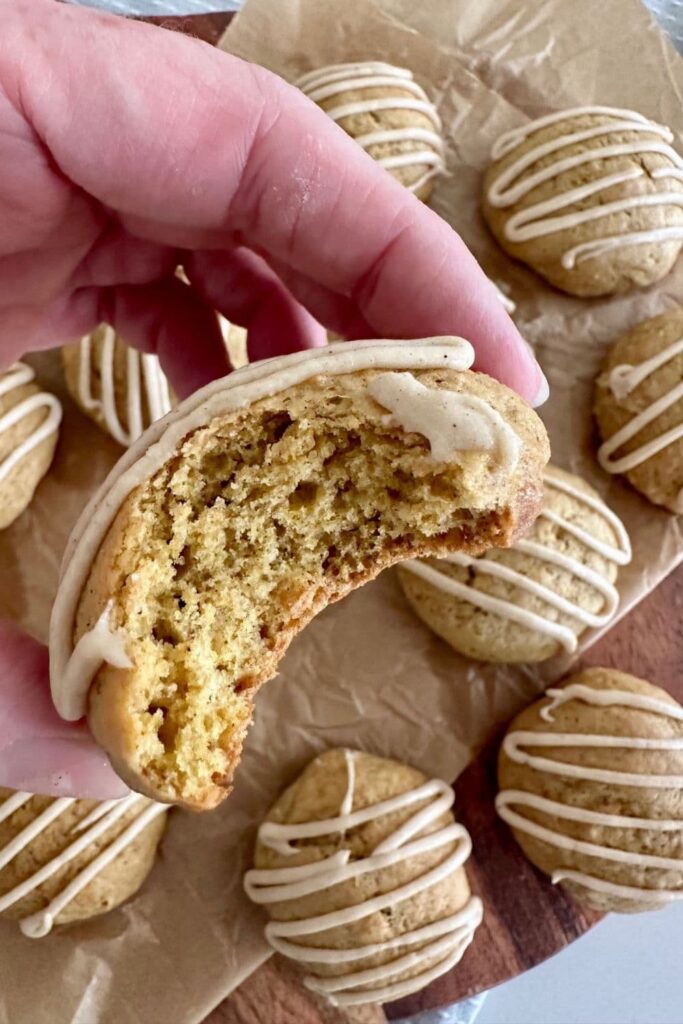 A soft sourdough pumpkin cookies that has been bitten into so you can see the soft texture inside. There are more whole cookies in the background.