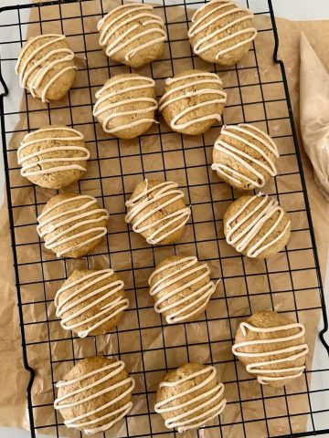 15 soft sourdough discard pumpkin spice cookies on a black wire cooling rack. There is a piece of parchment paper underneath the rack and a piping bag of glaze to the right.