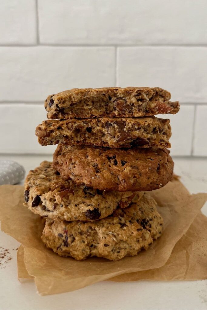 A stack of sourdough breakfast cookies sitting on a piece of parchment paper in front of a white tiled wall.