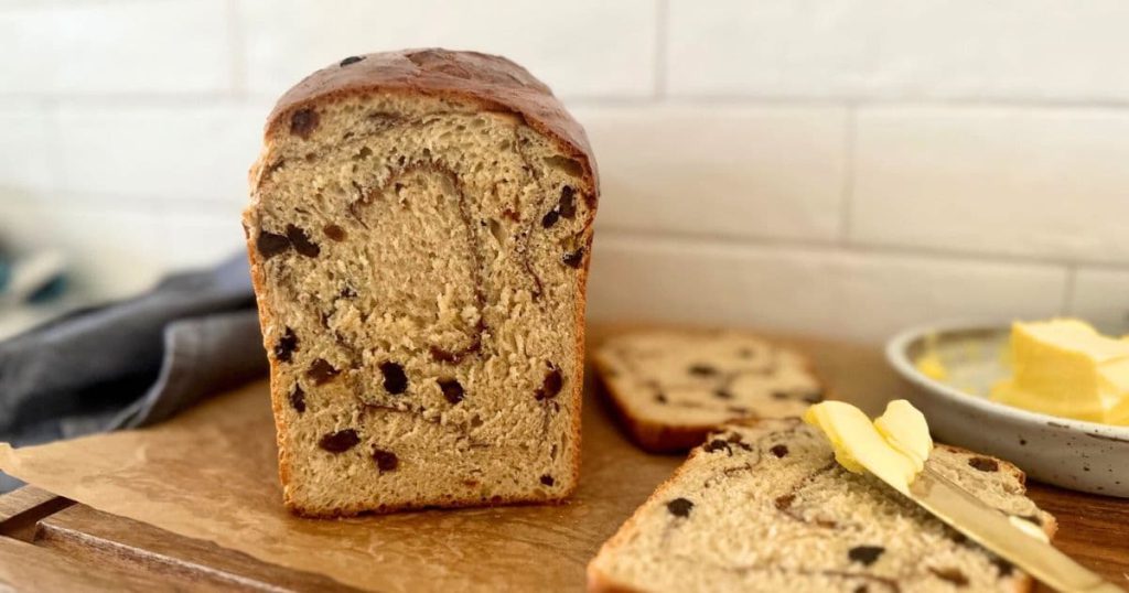 A loaf of cinnamon raisin bread that has been sliced and then positioned so you can see the crumb of the loaf.