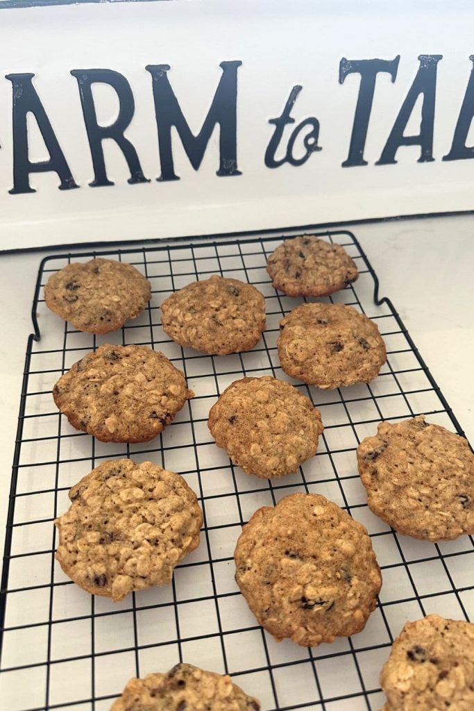 A black wire cooling rack with some sourdough oatmeal raisin cookies cooling. There is a farm to table sign in the background of the photo.