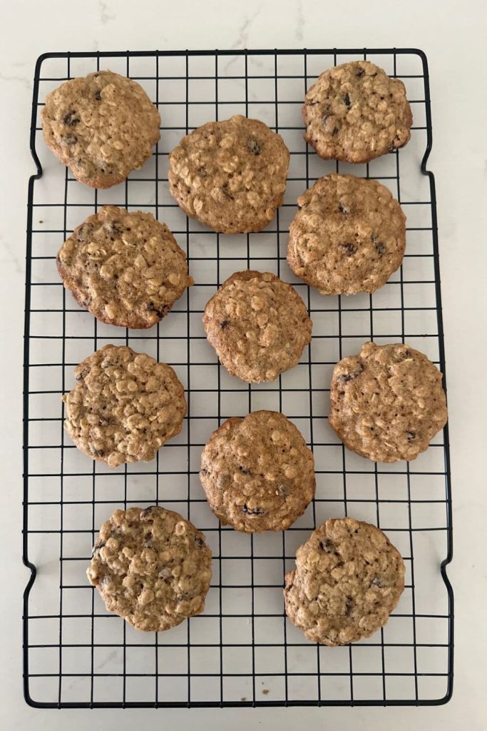 A black wire cooling rack with some sourdough oatmeal raisin cookies cooling. 