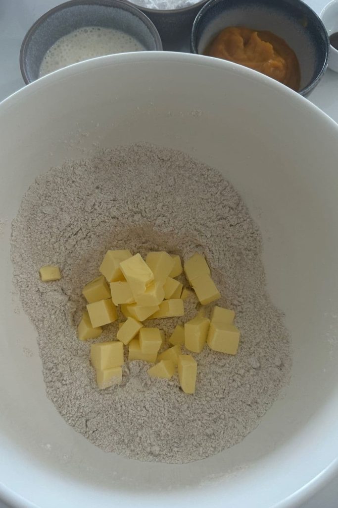 A bowl of the dry ingredients that have been mixed to combine. There are butter cubes sitting on the top of the dry ingredients in the bowl.