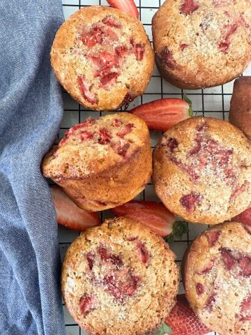 Sourdough Strawberry Muffins arranged on a black wire cooling rack. There is a blue dish towel sitting to the right of the muffins.