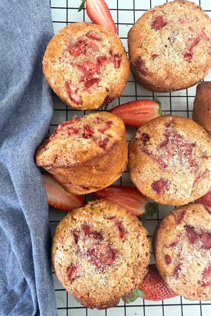 Sourdough Strawberry Muffins arranged on a black wire cooling rack. There is a blue dish towel sitting to the right of the muffins.