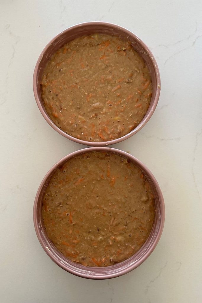 Two pink aluminum cake tins containing sourdough carrot cake batter.