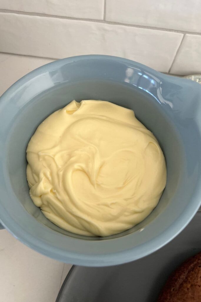 Blue batter jug containing vanilla cream cheese frosting for sourdough carrot cake.