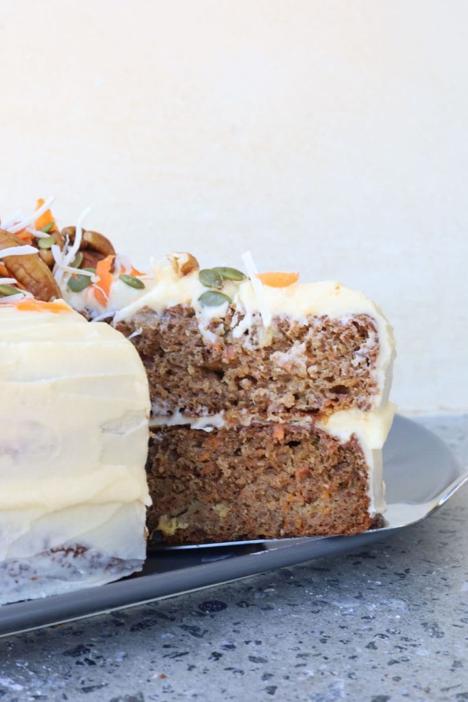 Up close photo of a sourdough carrot cake that has a slice pulled out so you can see the interior of the moist carrot cake.