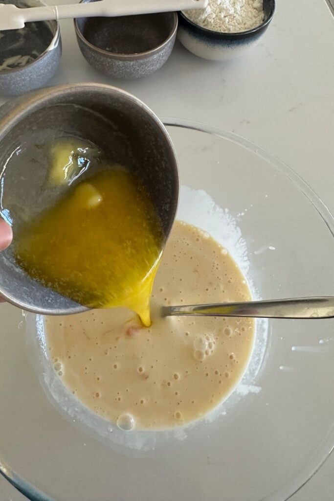 Adding melted butter to the sourdough cheese waffle mixture.