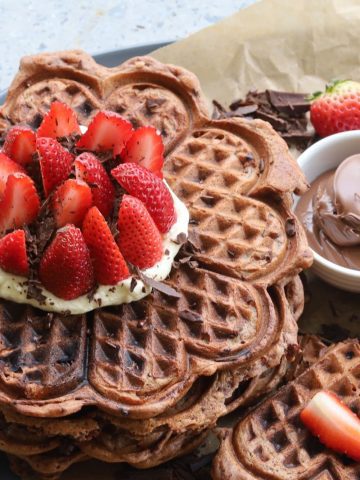Close up photo of a stack of sourdough chocolate waffles topped with whipped cream and strawberries.