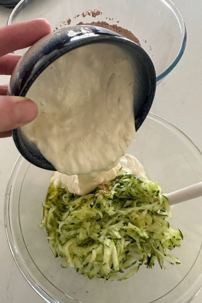 Pouring the sourdough starter into the shredded zucchini to make sourdough chocolate zucchini muffins.