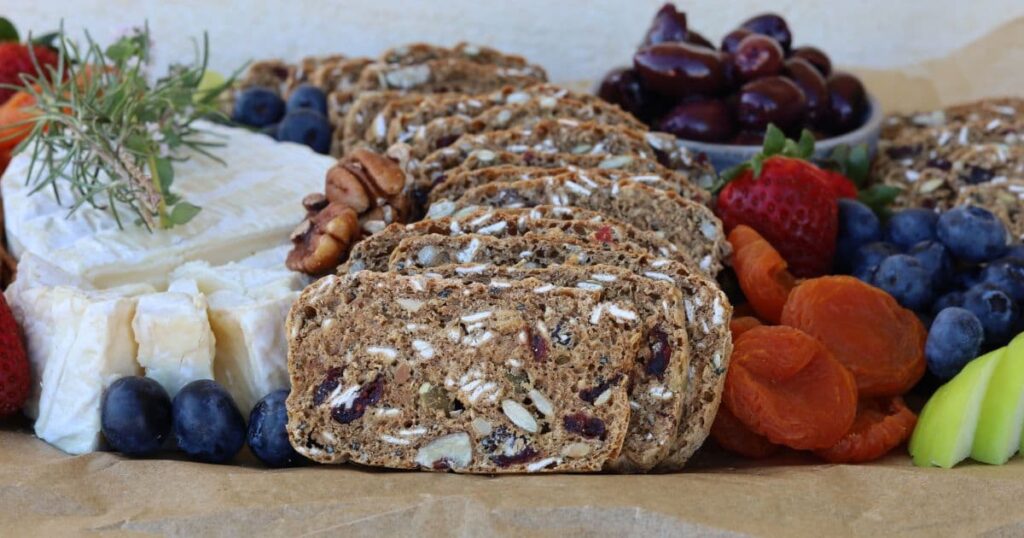 Sourdough Fruit and Seed crackers displayed on a cheese platter with soft French cheese, strawberries, apple, blueberries and olives.