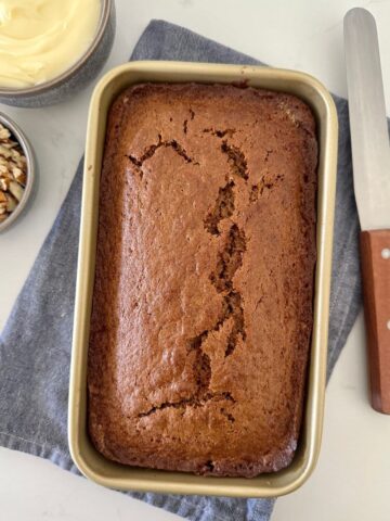 Sourdough gingerbread loaf in a gold loaf pan sitting on a blue dish towel. Sourdough gingerbread loaf is a type of sourdough quick bread.