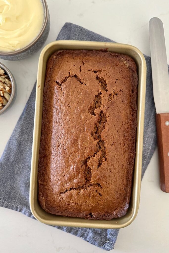 Sourdough gingerbread loaf in a gold loaf pan sitting on a blue dish towel. Sourdough gingerbread loaf is a type of sourdough quick bread.