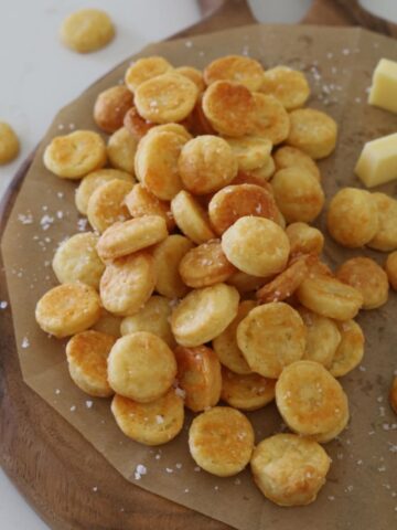 Sourdough Goldfish Crackers piled up on a wooden serving board. You can see the flaky sea salt that has been sprinkled over them.