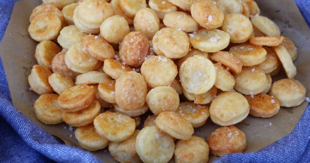 A big pile of sourdough goldfish crackers on a blue dish towel. They are topped with flaky sea salt.