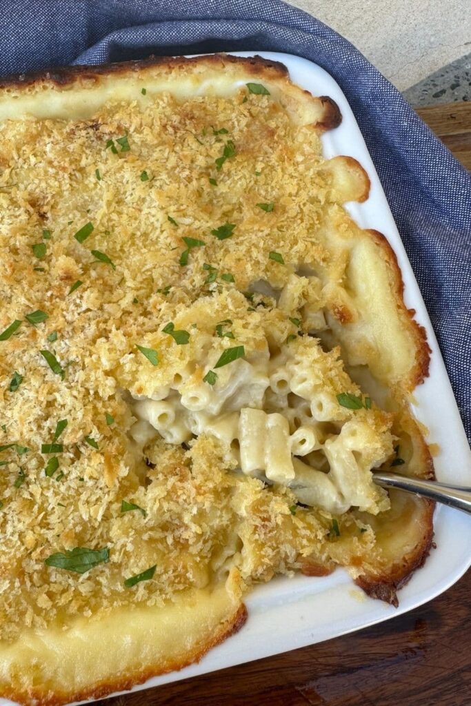 Sourdough mac and cheese baked in a white dish with breadcrumbs and parsley on top.