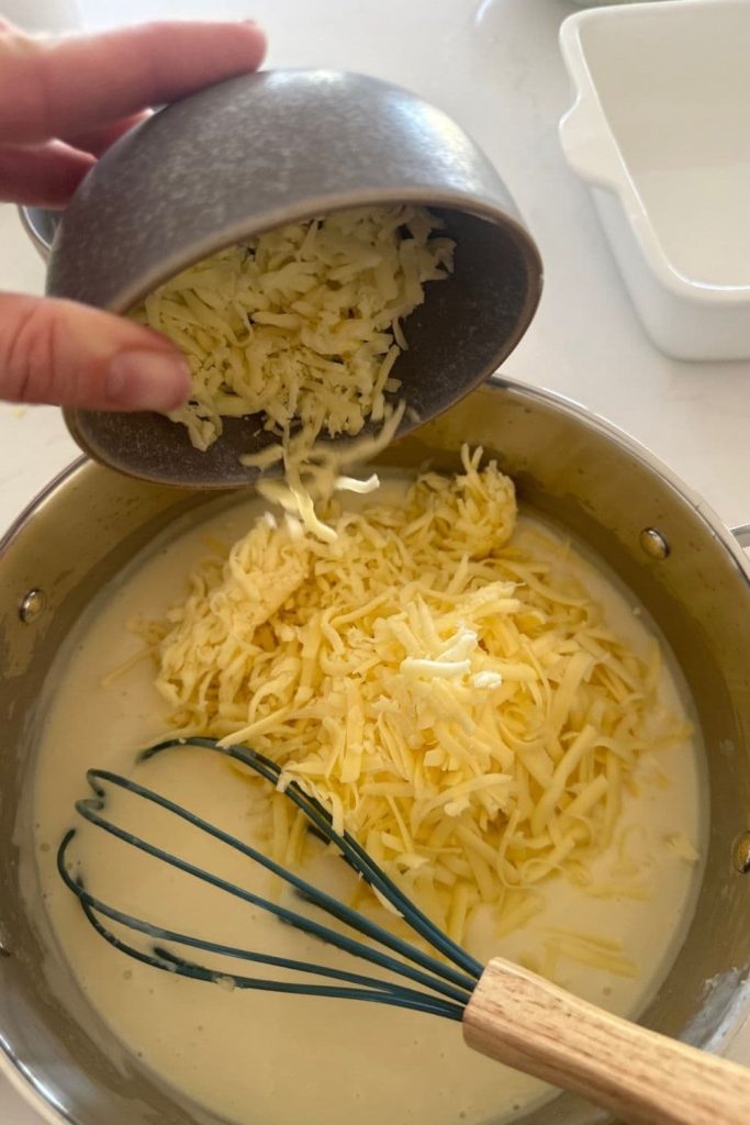 Cheese being added to sourdough white sauce when making sourdough mac and cheese.