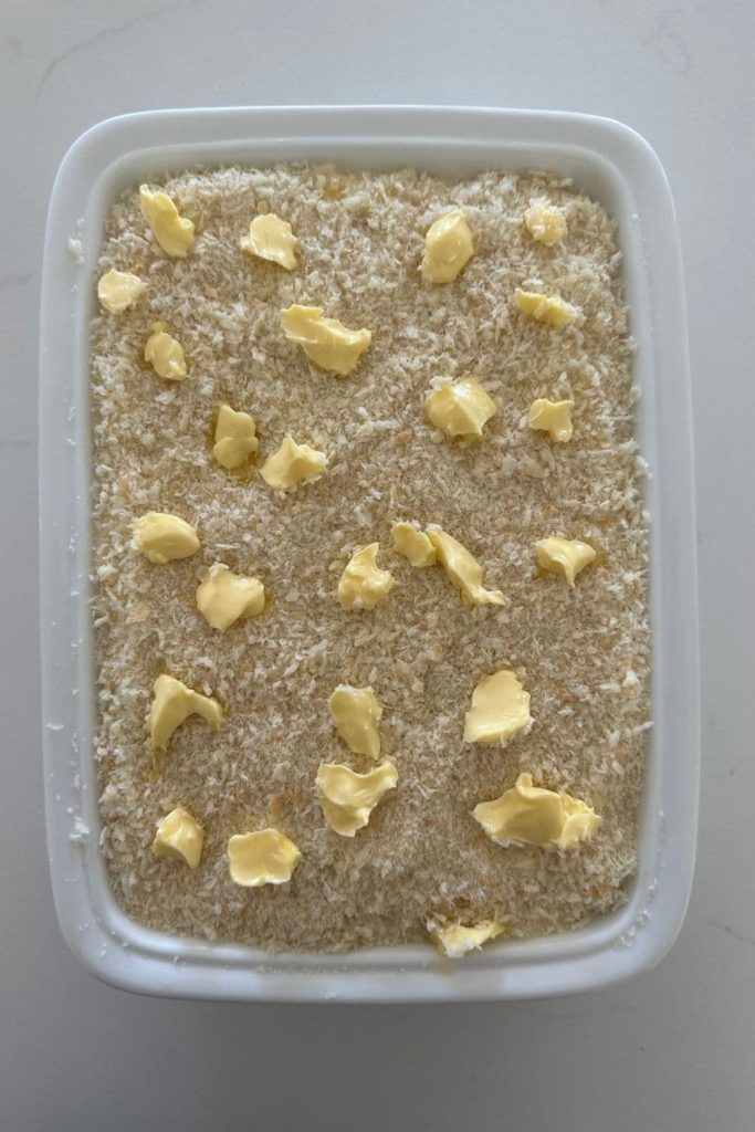 Sourdough mac and cheese in a white baking dish. The top has been covered in bread crumbs and knobs of butter.