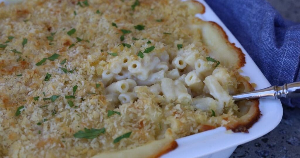 Sourdough mac and cheese served in a white rectangle dish. You can see the spoon digging into the creamy sauce. 