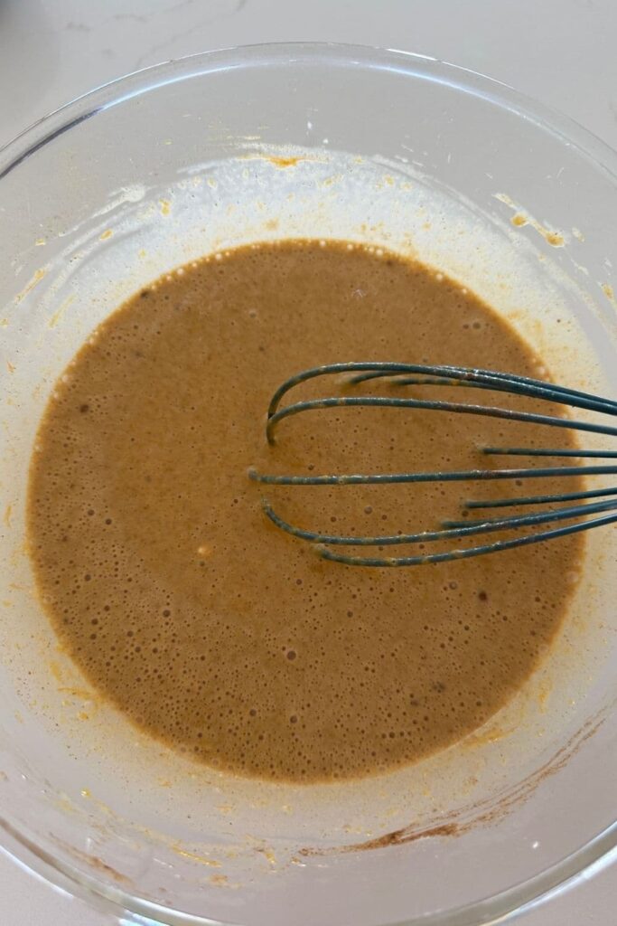 Pumpkin pie filling being whisked in a glass bowl.