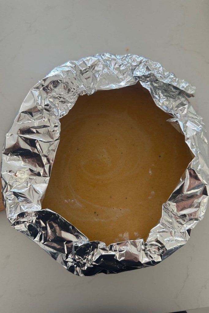 A photograph of a sourdough pumpkin pie shielded with aluminum foil to create a pie shield.