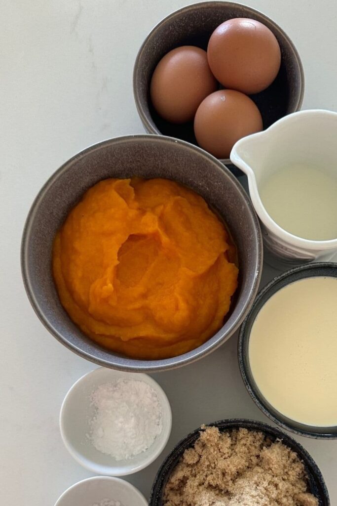 Bowl of homemade pumpkin puree sitting amongst other ingredients to make homemade sourdough pumpkin pie.