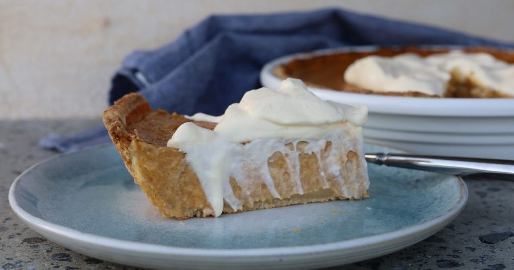 A slice of sourdough pumpkin pie served on a blue stoneware plate topped with whipped cream.