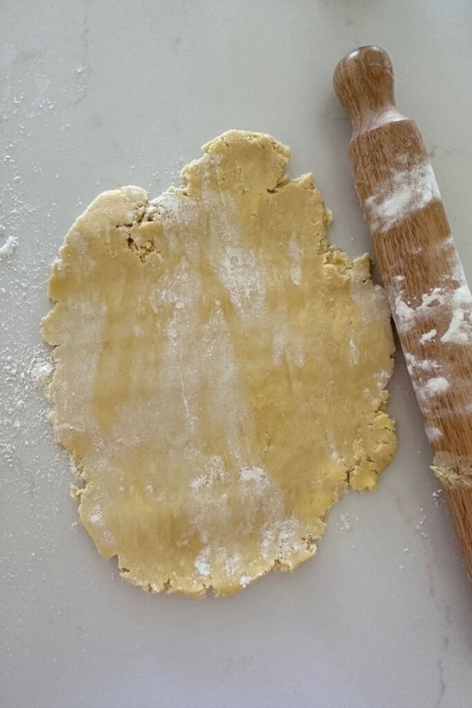 Sourdough pumpkin pie crust rolled out on a white counter top. There is a floured rolling pin sitting to the right of the pastry.