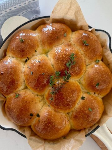 Sourdough skillet rolls bathed in honey thyme butter sitting in an enamel cast iron skillet.