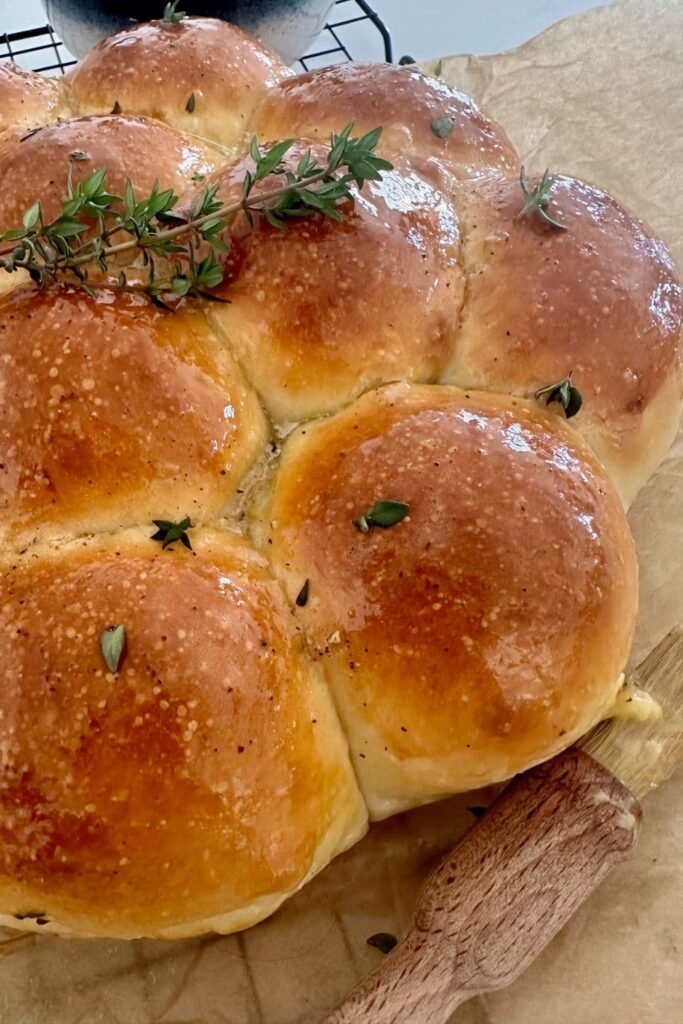 Close up photo of sourdough skillet rolls that have been taken out of the skillet and placed on a wire rack to cool. There is a pastry brush in the foreground of the photo.