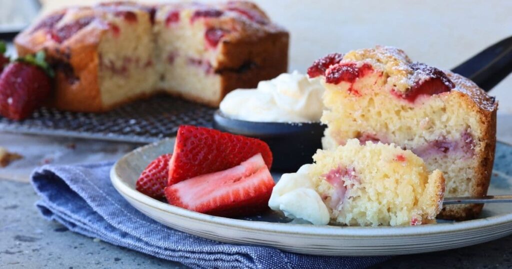 Sourdough Strawberry Cake served with homemade whipped cream and fresh strawberries on a blue stoneware plate.