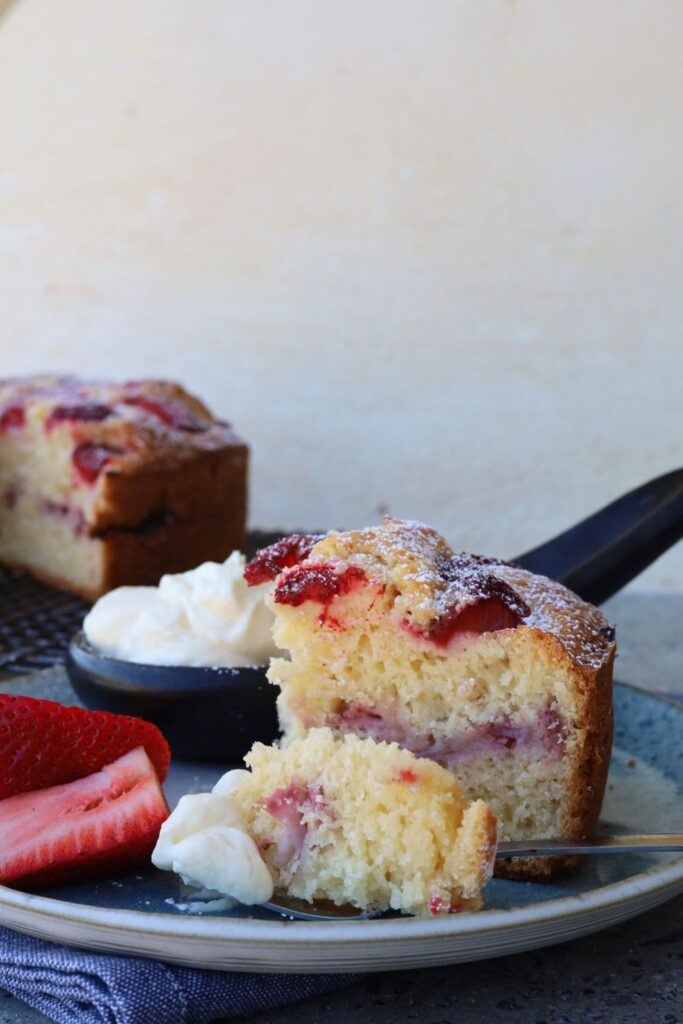 Sourdough Strawberry Cake served with whipped cream and fresh strawberries on a blue stoneware plate. You can see the rest of the cake in the background of the photo.