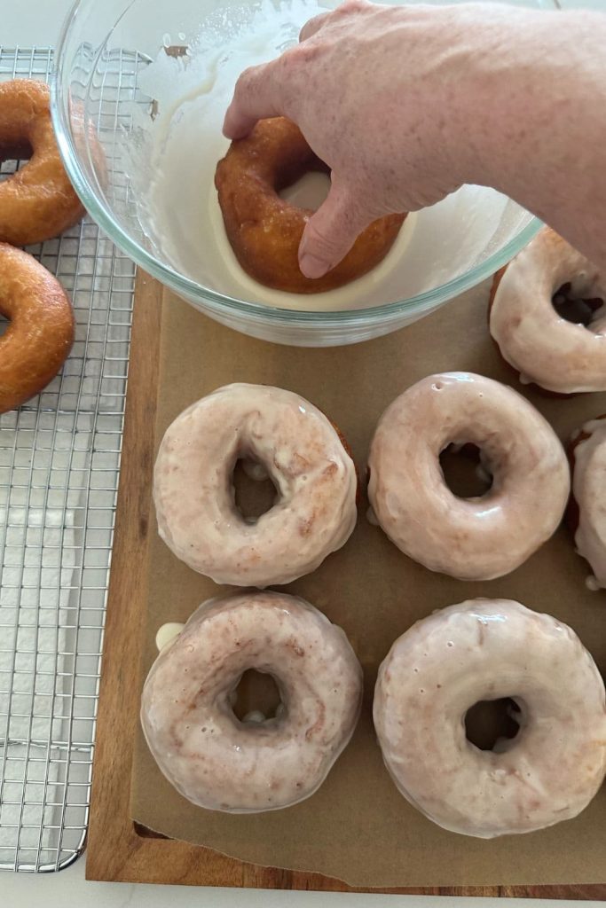 Dipping fried sourdough donuts in a vanilla glaze.