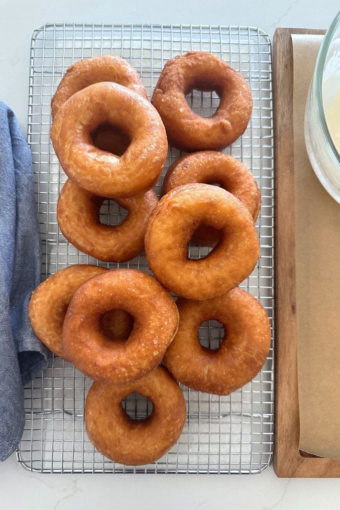 A batch of fried sourdough donuts sitting on a wire cooling rack ready to be dipped in vanilla glaze.