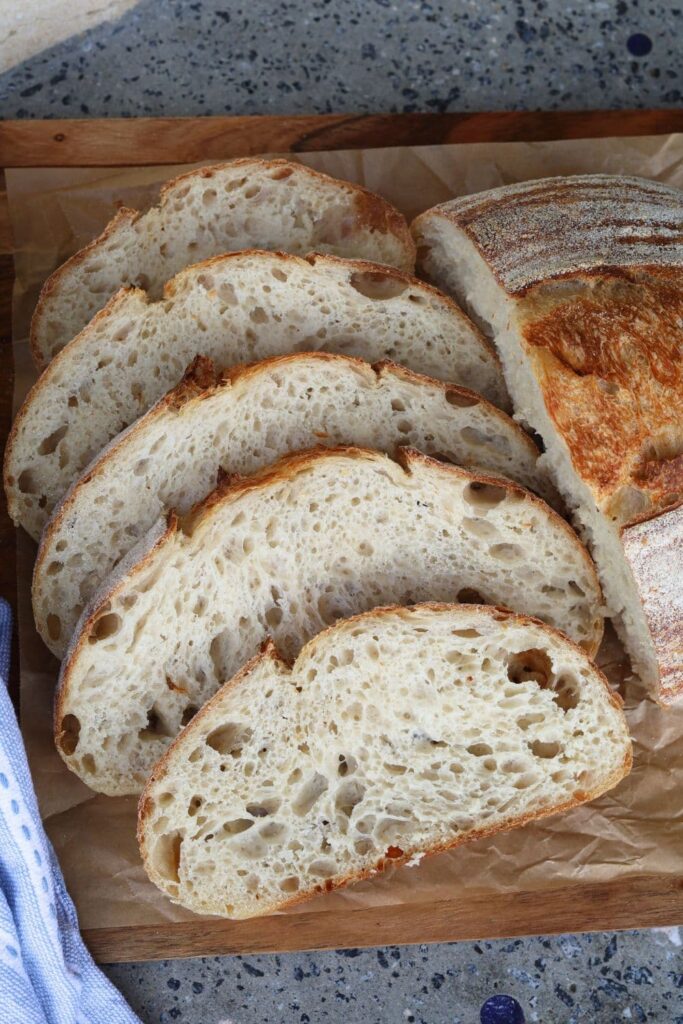 4 slices of higher hydration sourdough bread laid out on a wooden board. You can see the rest of the loaf sitting beside the slices.