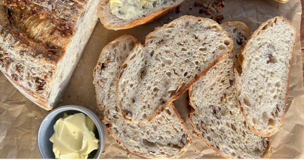 High protein sourdough bread displayed on a wooden board with a small dish of cultured butter.