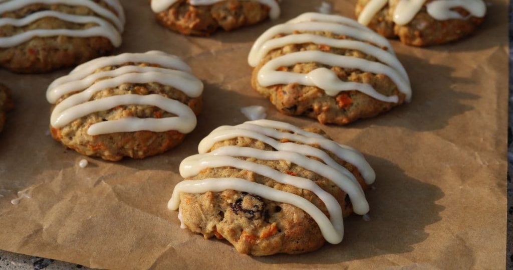 Sourdough carrot cake cookies that have been iced with a cream cheese glaze sitting on a piece of parchment paper.