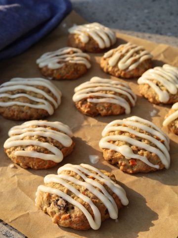 Sourdough carrot cake cookies that have been iced with a cream cheese glaze sitting on a piece of parchment paper.