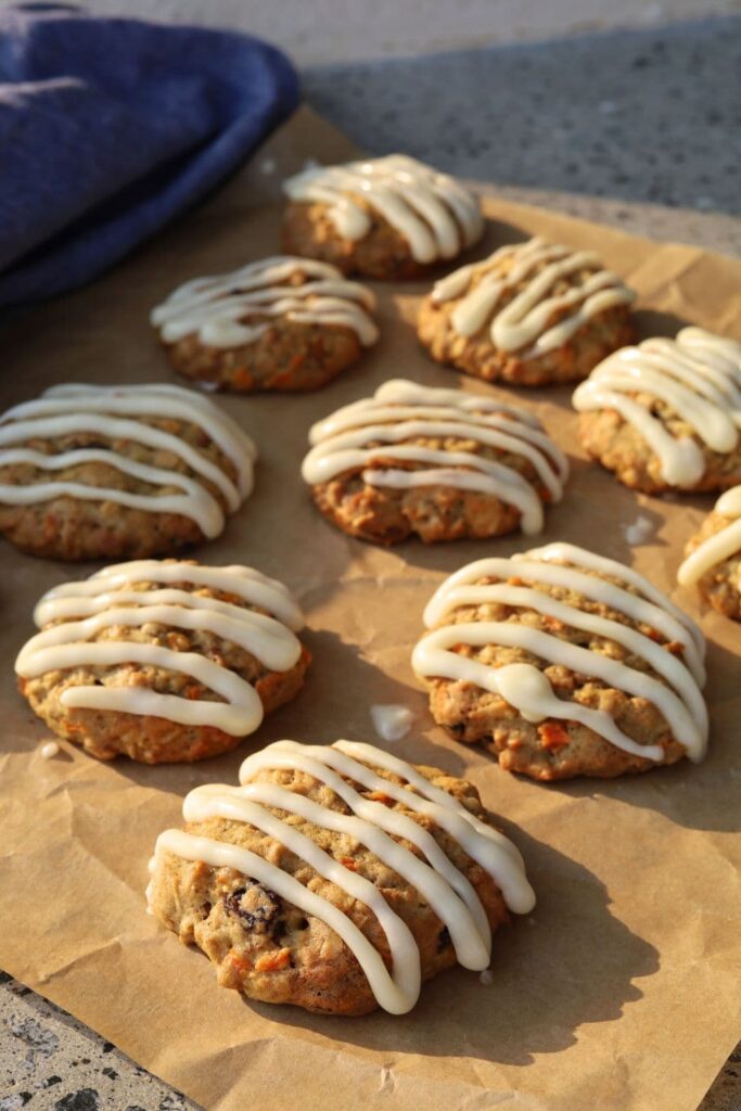 Sourdough carrot cake cookies that have been iced with a cream cheese glaze sitting on a piece of parchment paper.