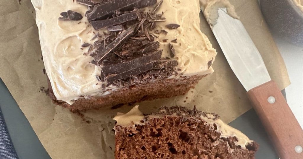 Sourdough Chocolate Chai Loaf Cake topped with chai spice vanilla cream cheese frosting and chopped chocolate. There is an offset spatula sitting the to the right of the loaf cake.