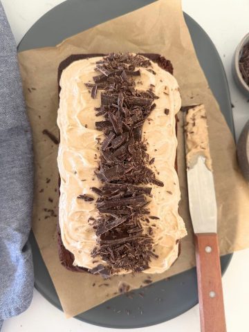 Sourdough Chocolate Chai Loaf Cake topped with chai spice vanilla cream cheese frosting and chopped chocolate. There is an offset spatula sitting the to the right of the loaf cake.