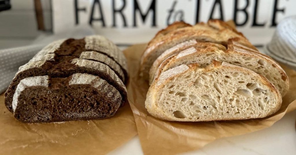 Two loaves of sourdough bread sitting on a piece of parchment paper. There is a sign in the background that says "farm to table". 