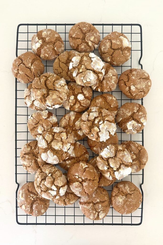 A batch of sourdough gingerbread crinkle cookies sitting on a black cooling rack.