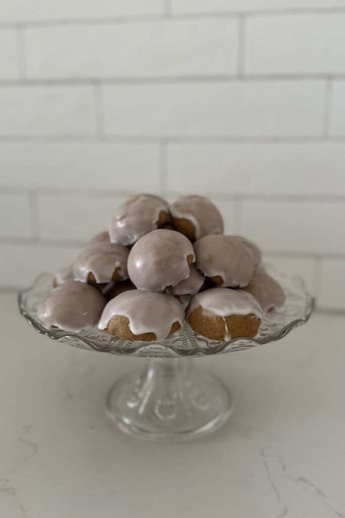 A pile of sourdough pfeffernusse cookies sitting on a glass cake plate.