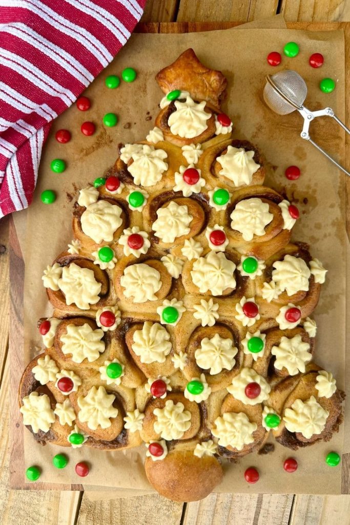 This sourdough Christmas Tree made with sourdough cinnamon rolls is one of the prettiest Christmas recipes. Cinnamon roll Christmas tree studded with vanilla cream cheese icing which has been piped on and decorated with red and green chocolate buttons.
